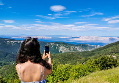 Woman on top of hill taking photos of view, landscape, nature, sea, summer.