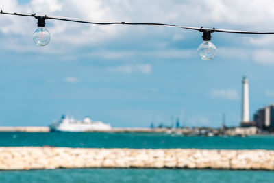 Vintage light bulbs with white clouds, blue sea and breakwater, bari port or harbor with lighthouse