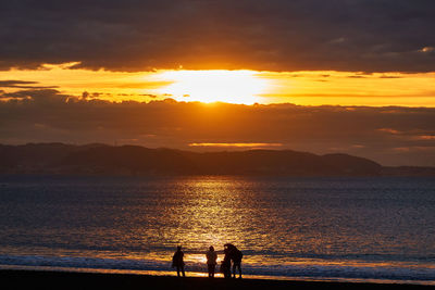 Silhouette people on beach against sky during sunset