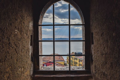 Houses by sea against cloudy sky seen through window of old building