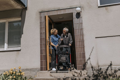 Female caregiver assisting senior man moving out with walker