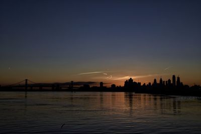Silhouette city by river against sky at sunset