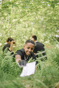 Smiling teenage boy picking up plastic from plant