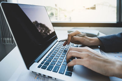 Cropped hands of businesswoman using laptop while sitting at office