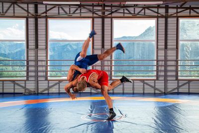 Two young men in blue and red wrestling tights are wrestlng and making shot through the thigh 