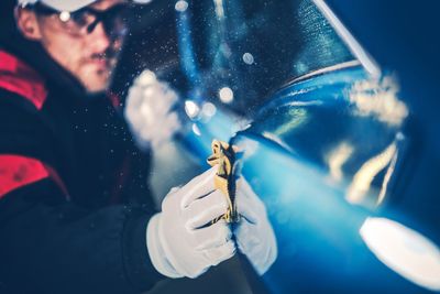 Male worker polishing blue car in factory