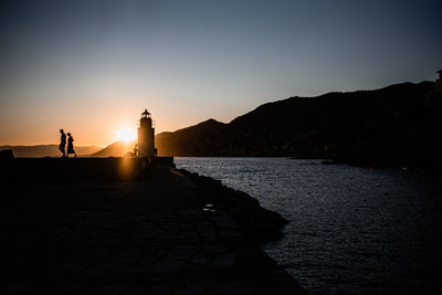 Silhouette people by sea against clear sky during sunset