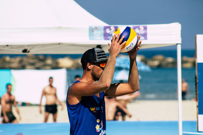 Man holding umbrella while standing against blue sea