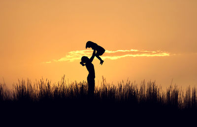 Silhouette woman lifting daughter on field during sunset