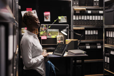 Side view of woman using laptop while standing in library