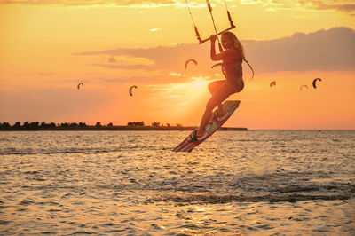 Silhouette person paragliding in sea against sky during sunset