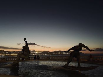 People at beach against clear sky during sunset