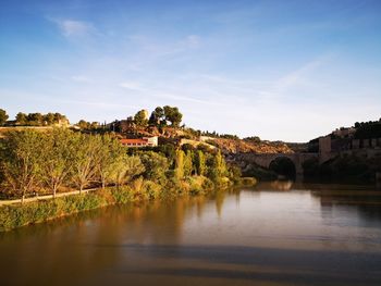 Arch bridge over river by buildings against sky