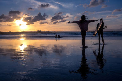 Men fishing on beach against sky during sunset