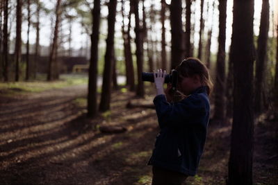 Side view of woman photographing at forest