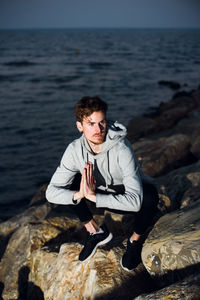 Full length of young man exercising on rock by sea
