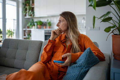 Side view of woman using mobile phone while sitting on sofa at home