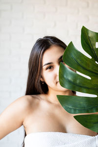  beautiful brunette woman wearing bath towels holding a green monstera leaf in front of her face