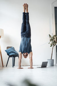 Man doing handstand by chair in front of wall at home
