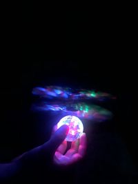 Close-up of hand holding illuminated light over black background