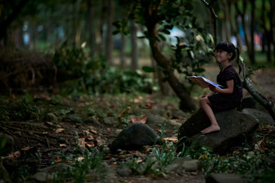 Little child reading a book in a green coastal forest