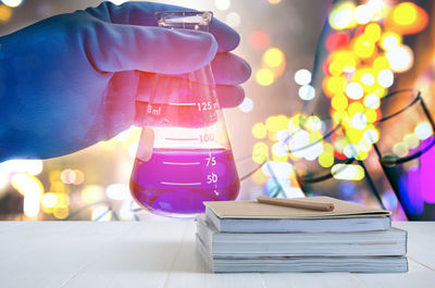 Cropped hand of scientist holding chemical in flask against illuminated lights