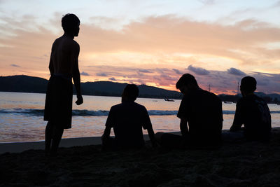 Men sitting at beach during sunset