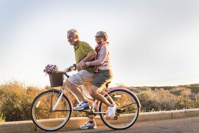 Couple riding bicycle on road against sky