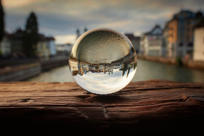 Close-up of crystal ball on water in city against sky