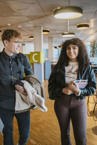 Portrait of smiling young woman walking with man at university cafeteria