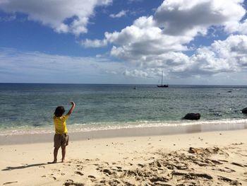 Rear view of woman walking on beach against sky