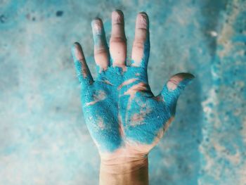 Cropped hand of man covered with blue powder paint against wall