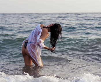 Side view of woman in sea against sky