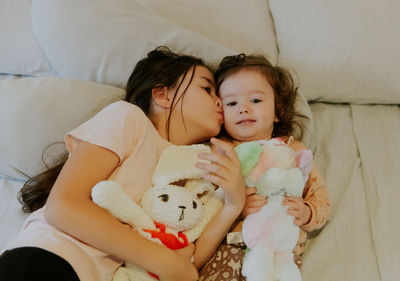 Two girls with toys lie on the bed in the morning.