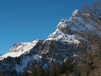 Low angle view of snowcapped mountains against clear blue sky