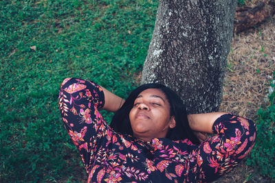 High angle view of smiling young woman lying down on tree trunk