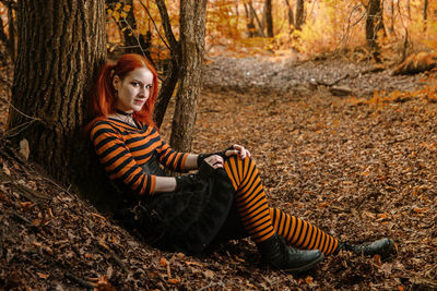 Portrait of smiling young woman sitting on tree trunk in forest