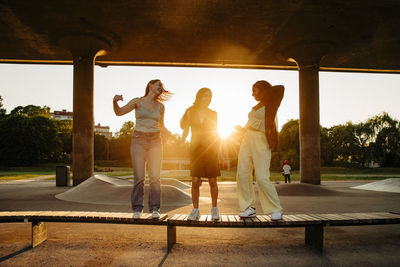 Happy teenage girl dancing on bench while enjoying under bridge during sunset