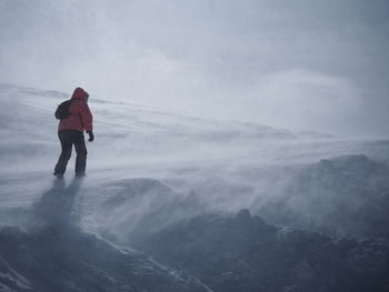 Rear view of man on mountain against sky during winter