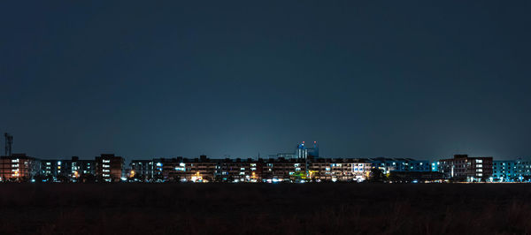 Illuminated buildings in city against clear sky at night