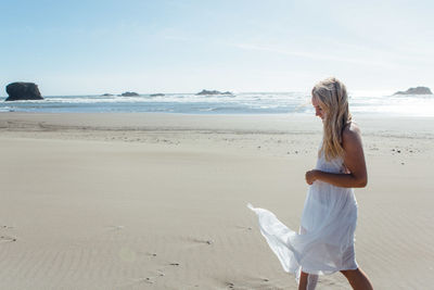 Side view of smiling young woman walking on beach against clear sky