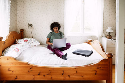 High angle view of young woman using laptop while relaxing on bed at home seen through doorway