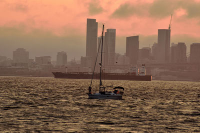 Ship in sea against buildings during sunset