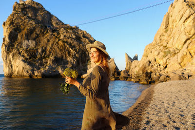 Portrait of woman standing at beach against rock formation