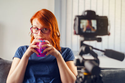 Portrait of woman holding camera while sitting at home