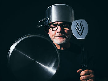 Portrait of man holding eyeglasses against black background