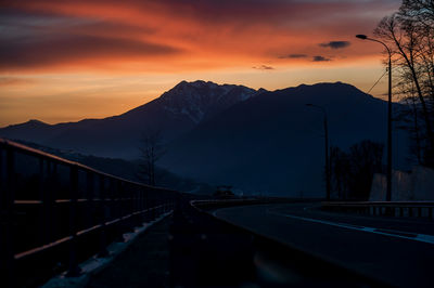 Road by silhouette mountains against orange sky