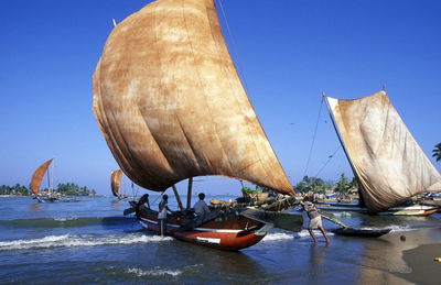 Fishermen with sailboats at beach against clear blue sky