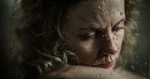 Close-up of sad young woman seen through wet glass window