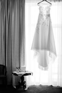 Wedding dress hanging against curtain next to personal accessories at round table